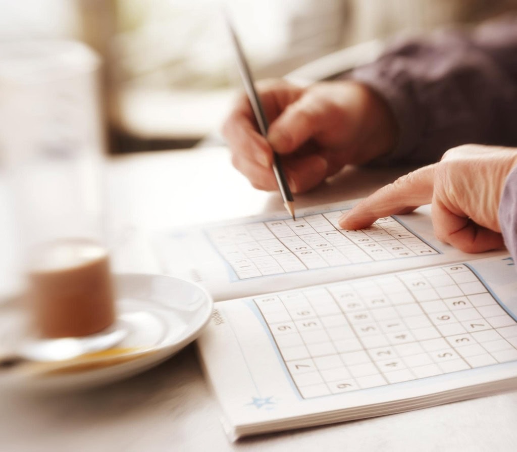 Hand writing in a Sudoku puzzle, focusing on brain games and recreational activities.